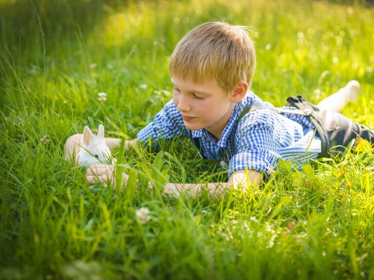 Ein glücklicher Junge spielt mit einem kleinen Kanninchen in der Wiese