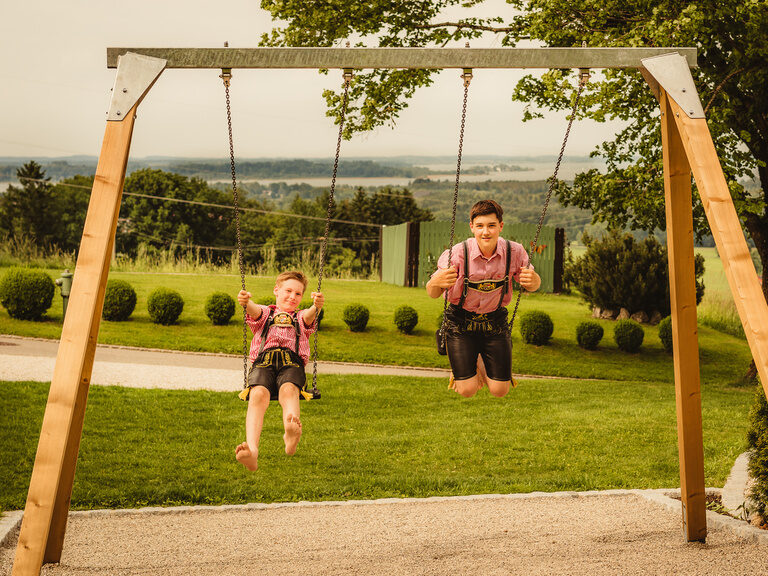 Zwei Jungen in Tracht schaukeln fröhlich im Garten