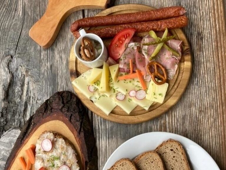 Ein Holztisch ist mit Wurstplatten und Brot für eine traditionelle Brotzeit gedeckt