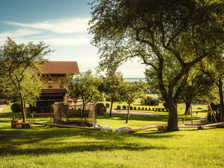 Der große grüne Garten mit Bäumen und dem Bauernhaus im Hintergrund.